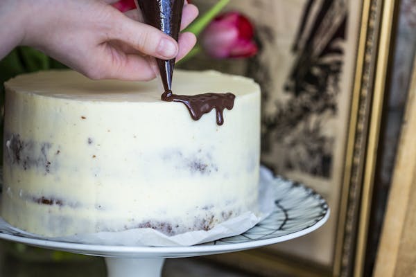 Ein heller Naked Cake wird mit einer dunklen Schokoladenganache aus einem Spritzbeutel dekoriert