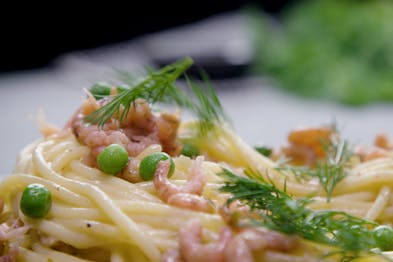 Eine Nahaufnahme von Spaghetti mit Krabben, Erbsen und Dill.