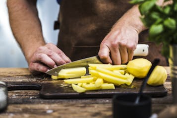 Hände, die Kartoffeln auf Holzbrett zu Pommes schneiden