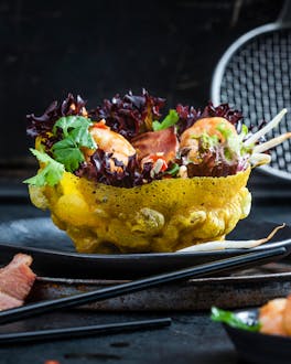 Goldgelbe vietnamesische Turbo-Teigschalen, die mit Salat und Garnelen gefüllt sind, vor schwarzem Hintergrund