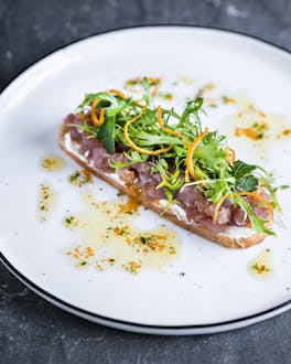 Thunfisch-Orangen-Tartar mit Salat und Brotchips auf weißem Teller vor grauem Hintergrund