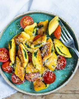 Mit Basilikumpesto gefüllte Gnocchi mit Tomaten und Parmesan auf türkisfarbenem Teller und Holztisch