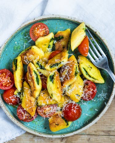Mit Basilikumpesto gefüllte Gnocchi mit Tomaten und Parmesan auf türkisfarbenem Teller und Holztisch