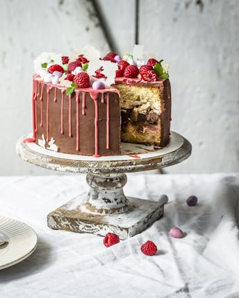 Angeschnittene Torte mit Rhabarberfüllung, einer Ganache aus dunkler Schokolade und pinkem Dripping, dekortiert mit Himbeeren.