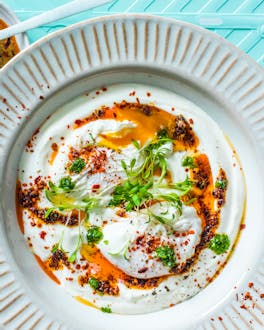 Türkische Eier aufJoghurt mit Chili-Butter und Petersilie vor türkisem Hintergrund