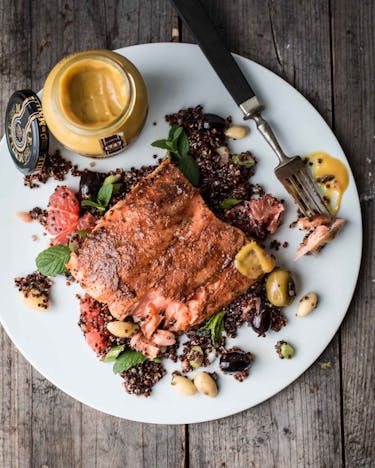 Auf einer Holzoberfläche steht ein Teller mit einer Portion Quinoa mit Lachs und Senf.