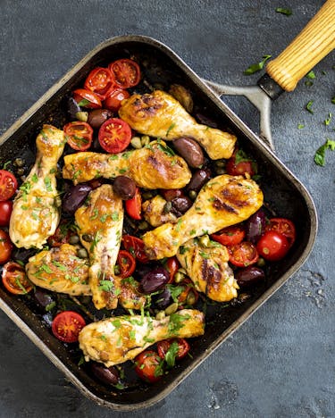 Pollo alla siciliana – Hähnchenkeulen mit Tomaten und Oliven in Pfanne auf grauem Untergrund