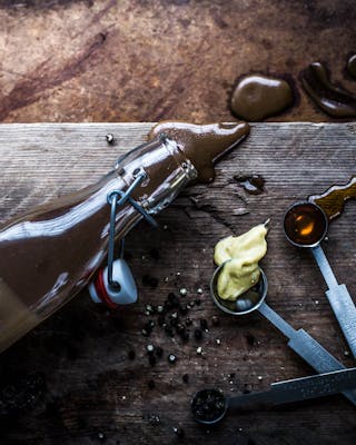 Eine umgekippte Balsamico-Dressing-Flasche liegt auf dunklem Holzuntergrund