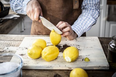 Eine Zitrone wird auf einem Holzbrett eingeschnitten. Daneben liegen vier weitere Zitronen.