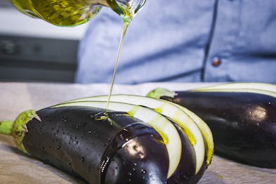 Aubergine als Fächer aufgeschnitten wird mit Olivenöl beträufelt