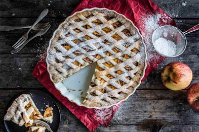 Der fertige Apple Pie steht auf Holzuntergrund, daneben ein Stück auf einem schwarzen Teller