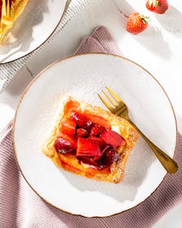 Vanille-Erdbeer-Plunder auf einer hellen gedeckten Kaffeetafel. Eine goldene Gabel liegt daneben.