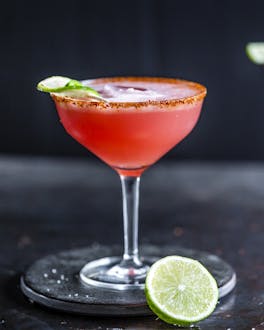 Zwei Margaritagläser mit roter Watermelon Margarita auf Eis, die mit Limettenschalen dekoriert sind