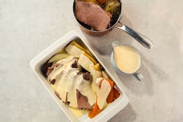 Tafelspitz, Gemüse und Sauce in einer weißen Auflaufform.Daneben stehen eine Sauciere und ein Topf mit Tafelspitz.