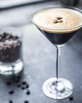 Espresso Martini auf dunklem Untergrund und Glas mit Kaffeebohnen im Hintergrund