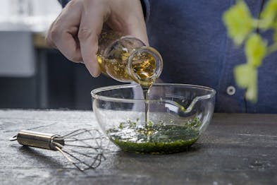 Olivenöl wird zum Kräuter-Dressing in Glasschüssel gegeben