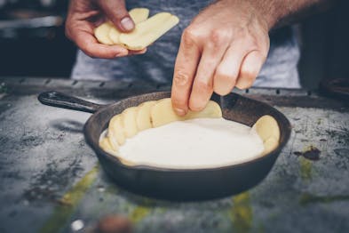 Eine Hand drapiert Kartoffelscheiben in einer Gusspfanne