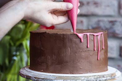 Dip Cake wird mit pinker Ganache aus einem Spritzbeutel dekoriert.