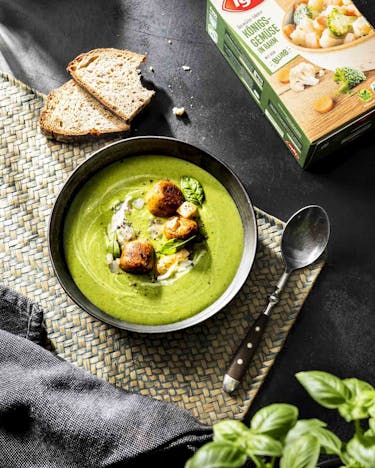 In einer dunklen Schale ist eine grüne Gemüse-Creme-Suppe gefüllt und mit veganen Hackbällchen getoppt.