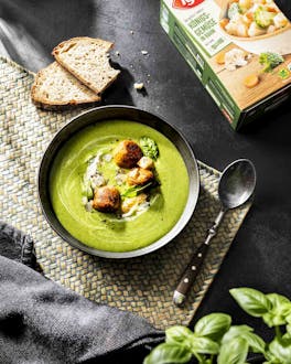 In einer dunklen Schale ist eine grüne Gemüse-Creme-Suppe gefüllt und mit veganen Hackbällchen getoppt.