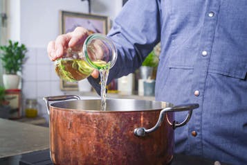 Koch gießt Weißwein aus Glasgefäß in Kupfertopf