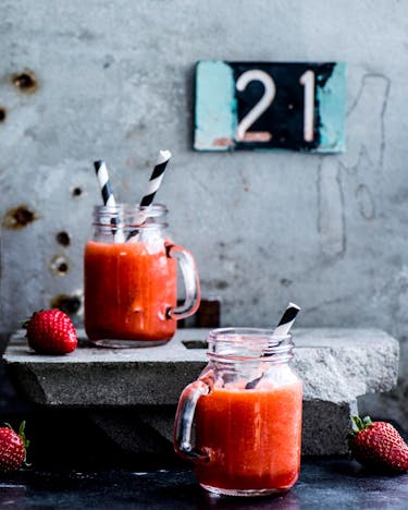 Erdbeerlimes in einer Flasche und in Gläsern abgefüllt mit Strohhalmen und einem Korken neben frischen Erdbeeren