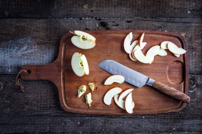 Auf einem dunklen Holzbrett liegen geschnittene Apfelspalten, daneben ein Messer