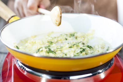 Zwiebeln werden in einer hellen Pfanne auf einer roten Kochplatte angedünstet.