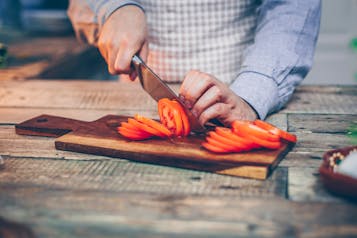 Auf einem Holzbrett wird eine Tomate in Scheiben geschnitten.