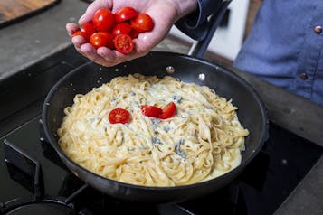 Pasta mit Gorgonzola wird mit Tomaten in Pfanne garniert
