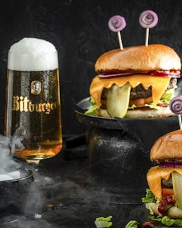 2 Monster-Burger und ein Glas Bitburger-Bier stehen vor schwarzem Hintergrund