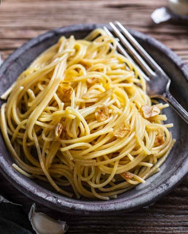Spaghetti aglio e olio mit Knoblauchchips auf grauen Teller mit dunklem Holzuntergrund