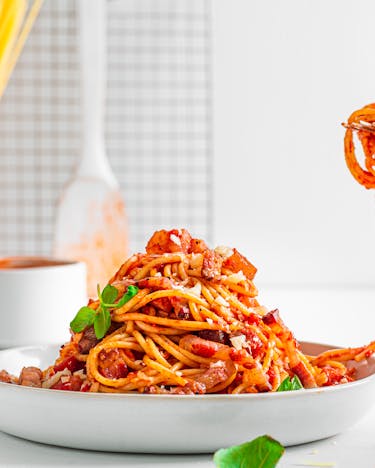 Spaghetti all'Amatriciana auf Teller, eine Gabel rollt etwas davon auf