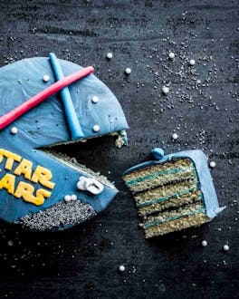 Angeschnittene blaue Star-Wars-Torte mit Laserschwertern und Star Wars Schriftzug auf dunklem Untergrund