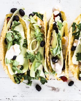 Tacos mit Bohnen und Paprika-Joghurt, nebeneinander angerichtet auf hellem Untergrund, von oben fotografiert.