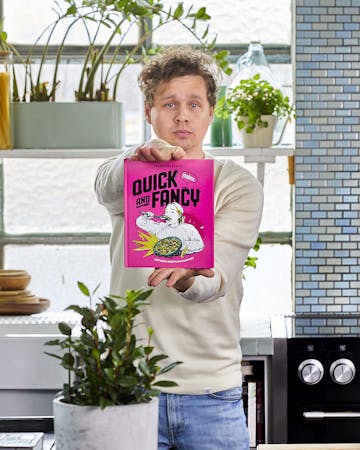 Hannes hält sein neues Kochbuch in die Kamera. Dabei steht er in der Küche.