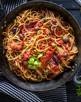 Spaghetti mit Tomatensauce im Topf auf schwarzem Hintergrund