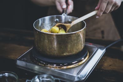 Mirabellen werden mit einem Holzlöffel in einem Topf auf einer Kochplatte eingekocht