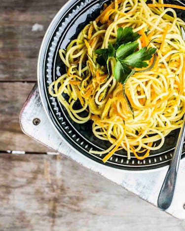 Schwarz-weiß gemusterter Teller mit Spaghetti, Möhrenstreifen und Petersilie auf Holzuntergrund
