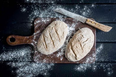 Auf einem Holzbrett liegen zwei ungebackene Laibe Brot