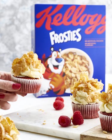 Red Velvet Cupcakes mit Cornflake-Topping und frischen Himbeeren vor einem hellen Hintergrund