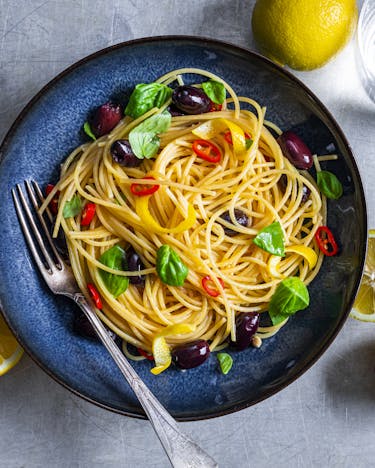 Spaghetti mit Zitrone und Basilikum auf blauen Teller und halbierten Zitronen daneben