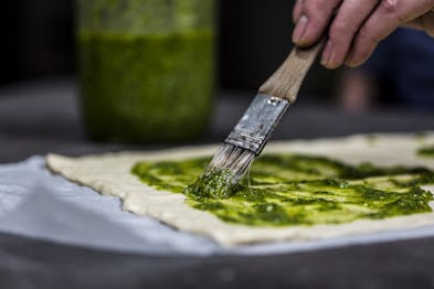 Pizzateig wird mit grünem Pesto bestrichen.