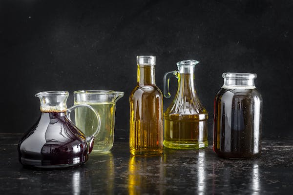Fünf unterschiedliche Glaskaraffen und -flaschen mit flüssigen Speiseölenin einer Reihe vor dunklem Hintergrund