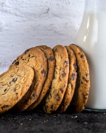 Chocolate Chip Cookies aneinander gereiht mit einer Glasflasche Milch.
