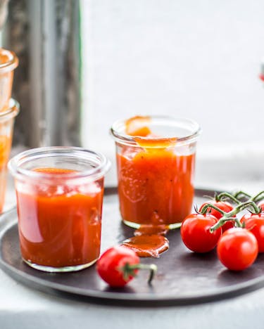 Tomatenketchup in Flasche und Gläser gefüllt mit Tomaten vor Fenster