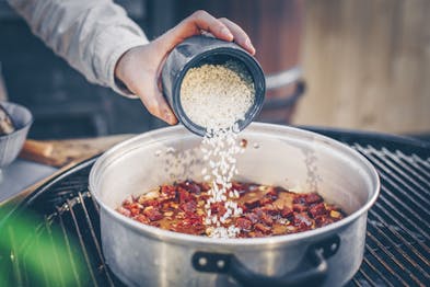 Chorizo, Zwiebeln und Knoblauch braten in einem Topf, Reis wird dazugegeben
