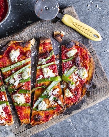 geschnittene Pizza mit grünem Spargel, Tomatensauce und Ricotta auf Holzbrett