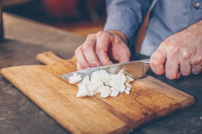 Mozzarella wird mit Messer auf Holzbrett gewürfelt