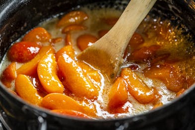 Aprikosenstücke werden in einem Kochtopf mit einem Holzlöffel verrührt